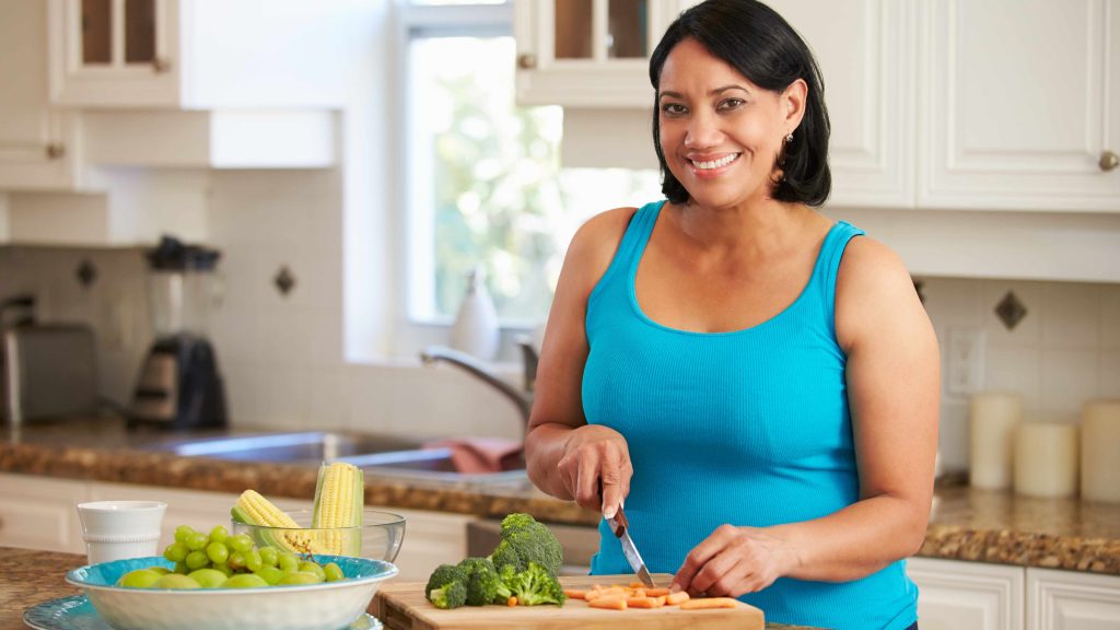 a smiling, overweight middle-aged woman preparing food in a kitchen