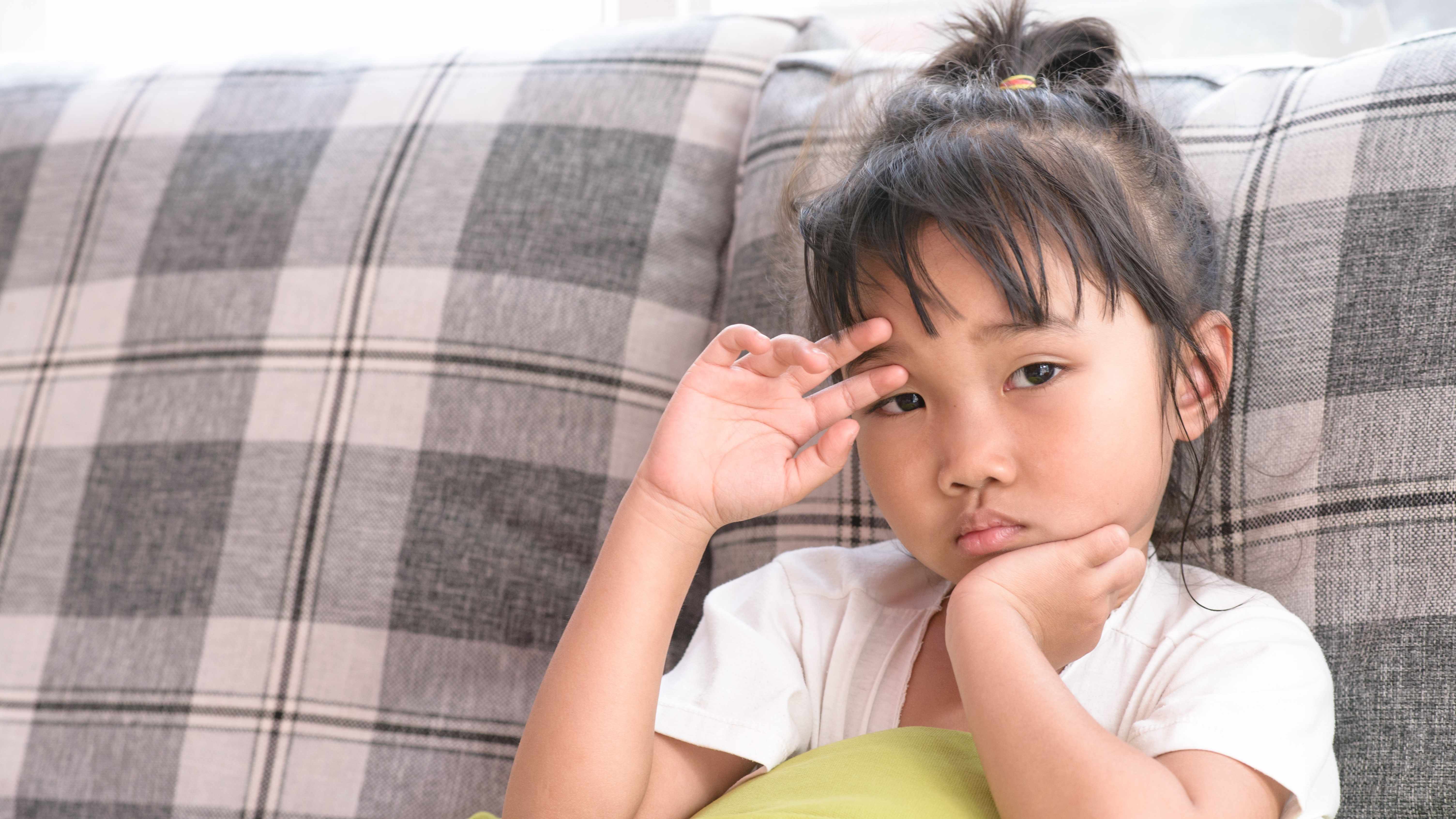 a young girl sitting on a couch, looking sad, worried or sick