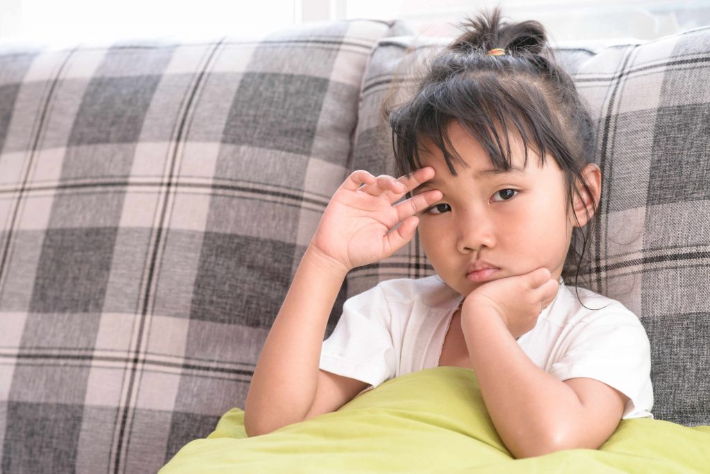 a young Asian girl sitting on a couch, looking sad, worried or sick