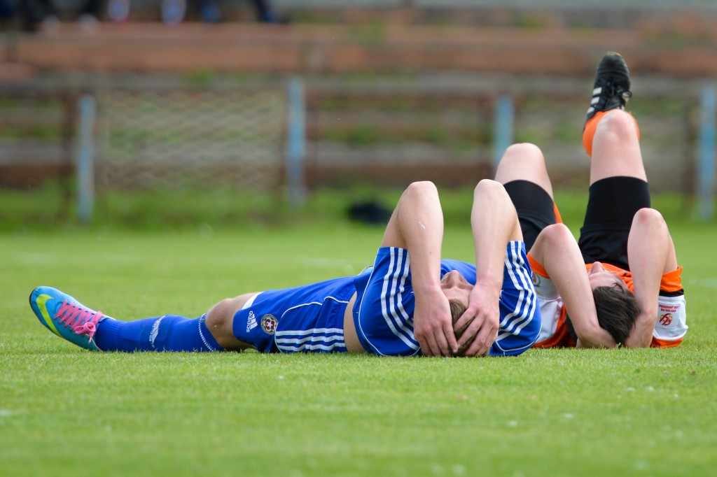 athletes on soccer sports field holding injured heads, perhaps concussions