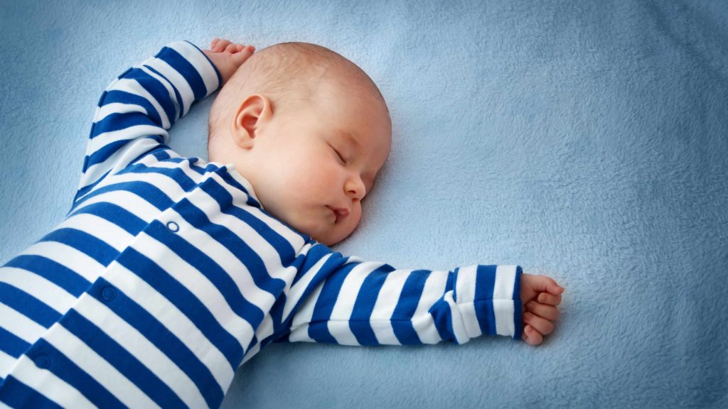 baby sleeping on his back in a crib with blue sheets
