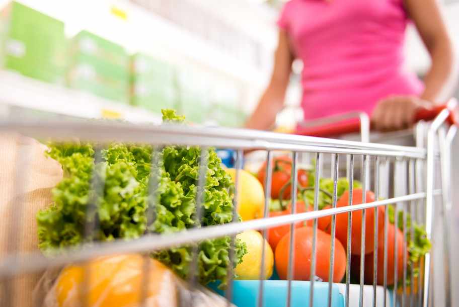 a woman pushing a shopping cart in the store, filled with vegetables for healthy eating