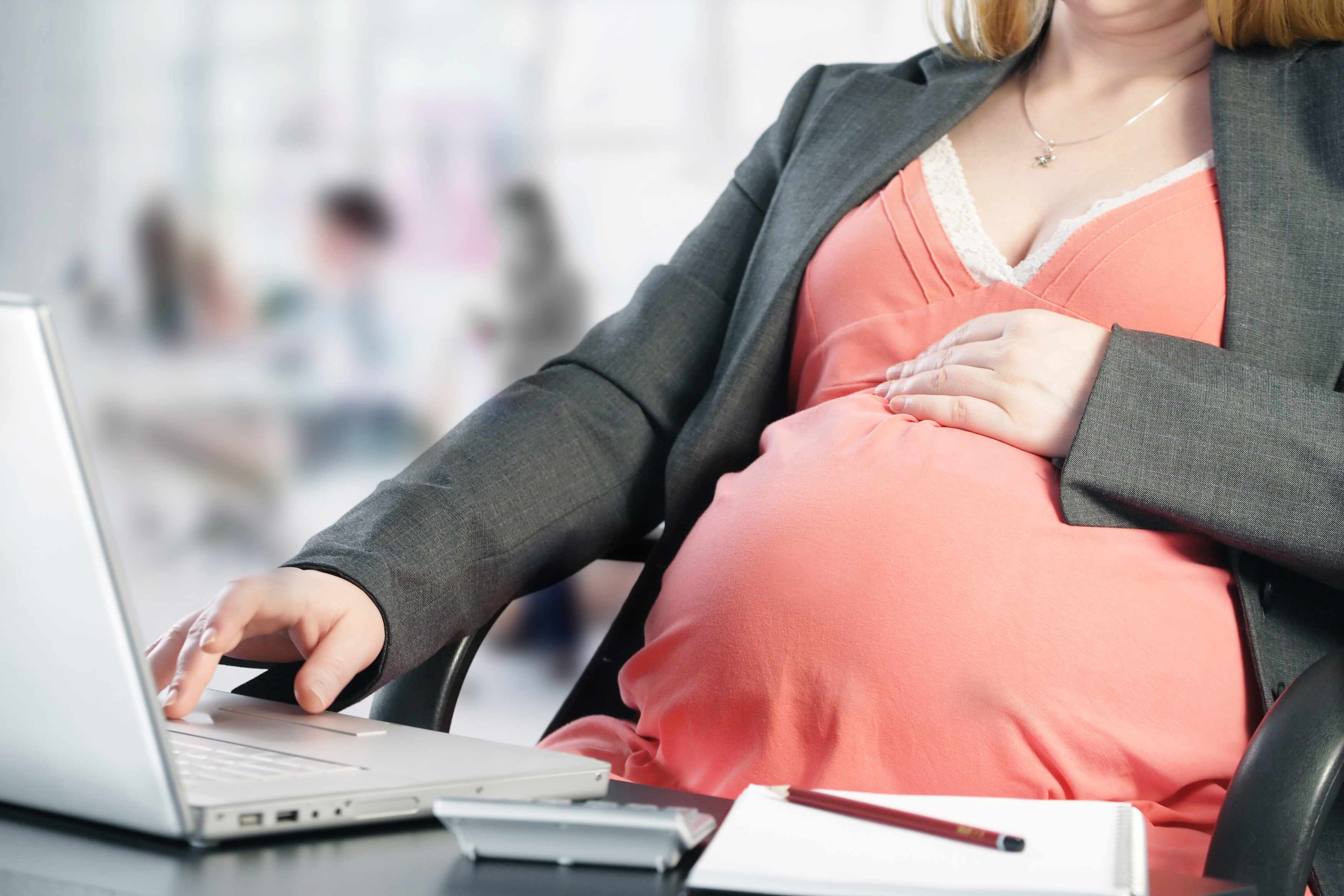 a young pregnant woman sitting at work on a laptop computer