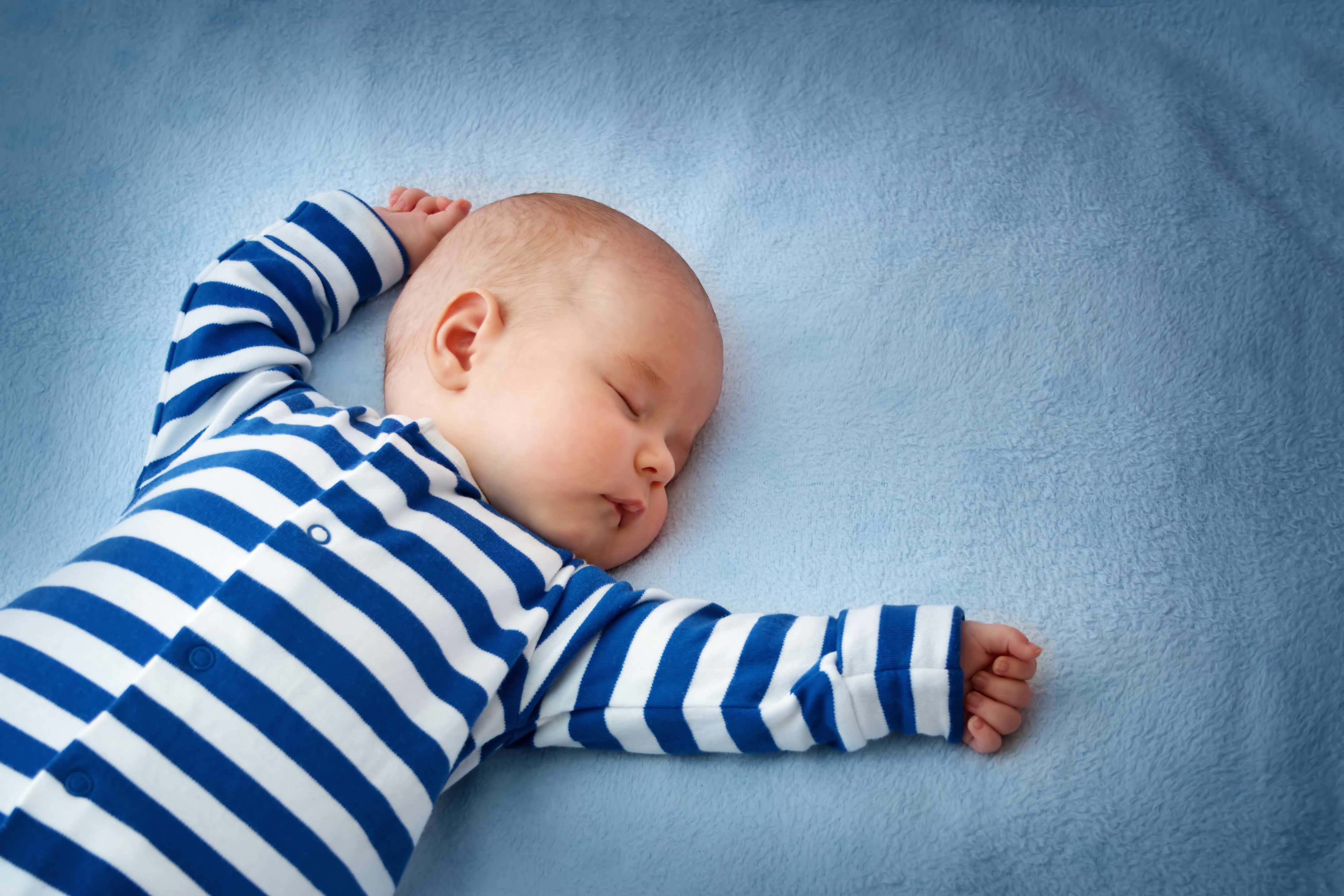 baby sleeping on his back in a crib with blue sheets