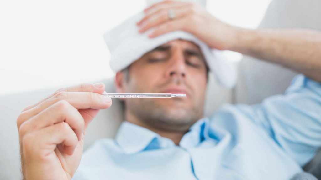 a sick man with cold or flu lying on sofa checking his temperature for a fever