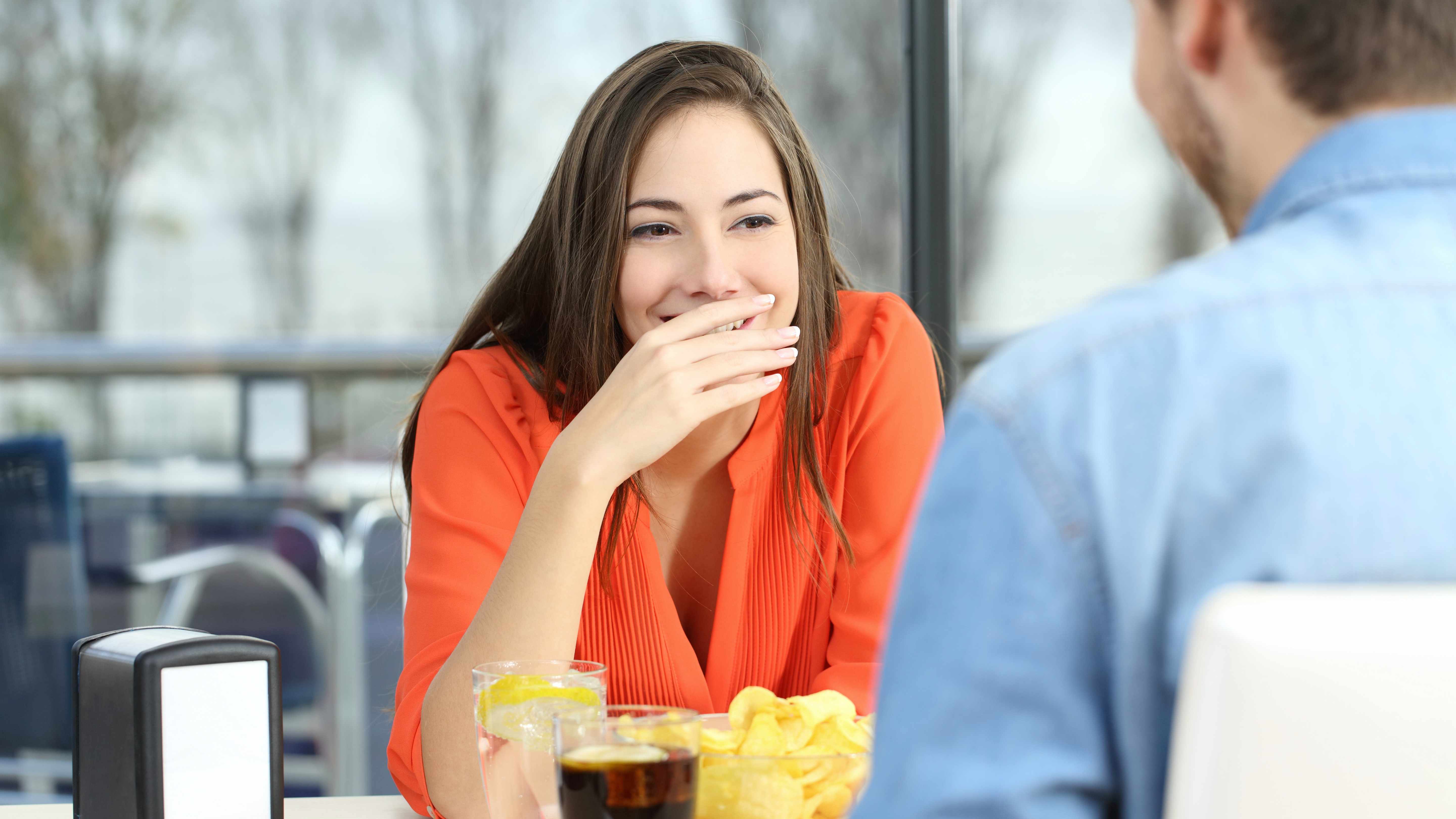 a couple sitting at a table and woman covering her mouth because of bad breath