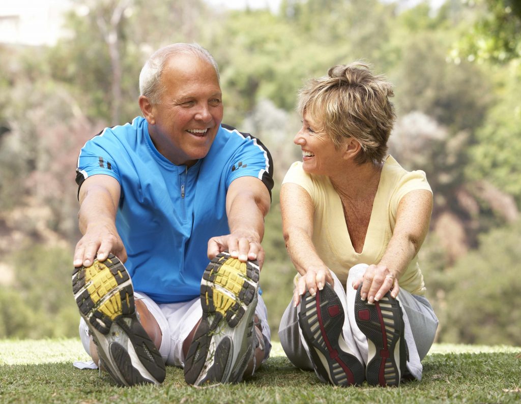 a middle-aged man and woman smiling and exercising in the park