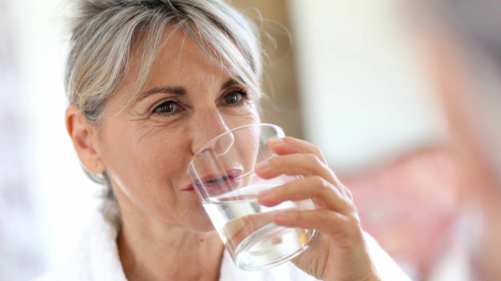 a middle-aged woman drinking a glass of water to stay hydrated