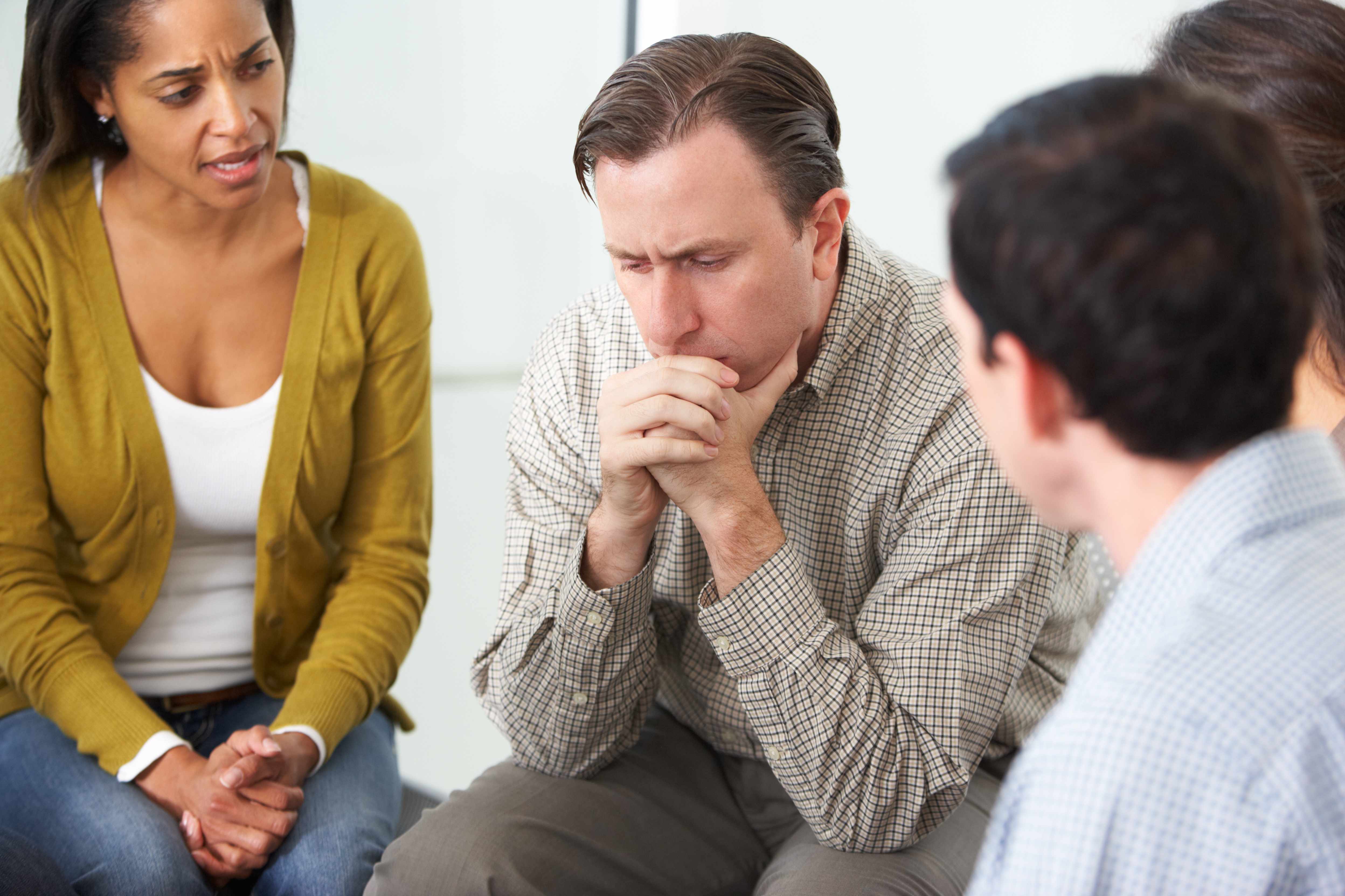 a man in a counselling session looking sad and depressed with concerned people sitting around him