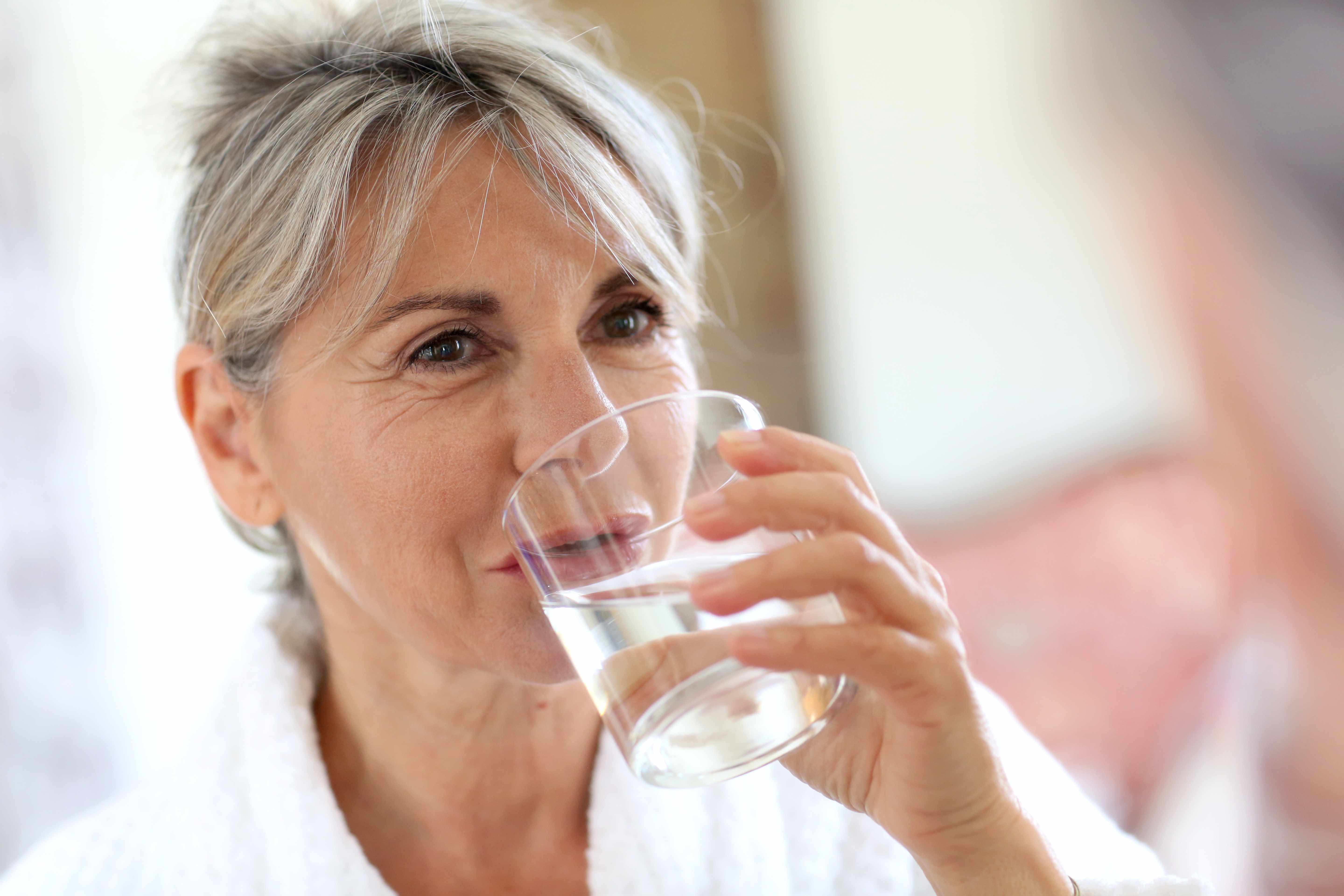 a middle-aged woman drinking a glass of water to stay hydrated