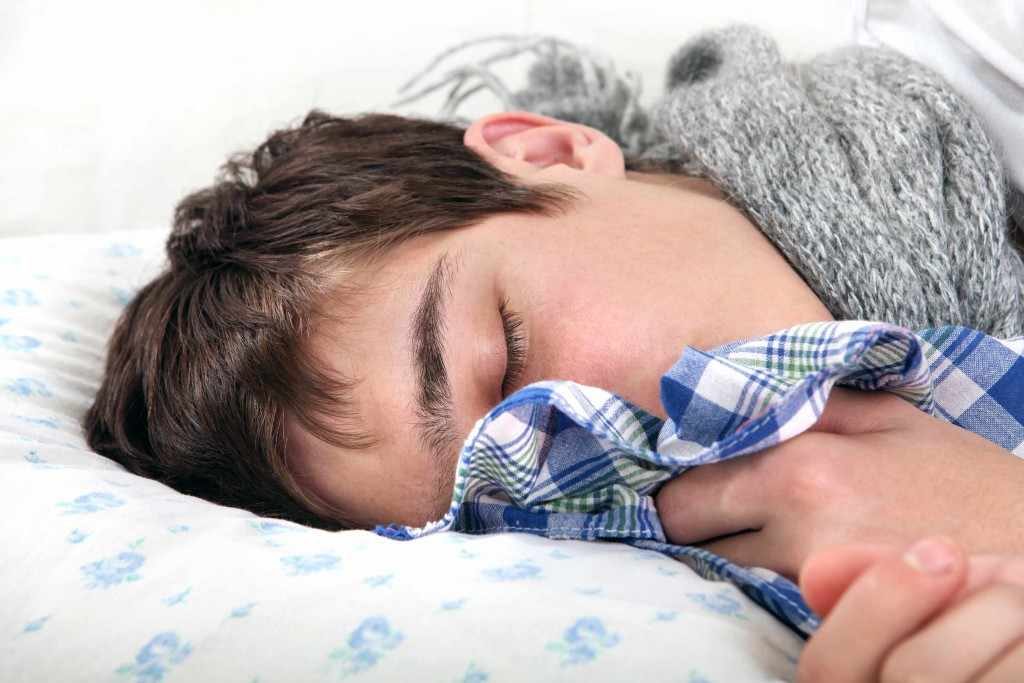 a teenage boy in bed looking sick with flu or cold