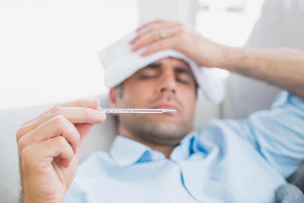 a sick man with cold or flu lying on sofa checking his temperature for a fever