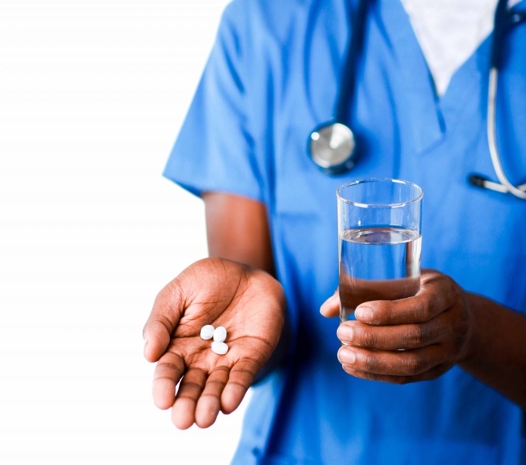 a medical staff person holding medication pills and a glass of water