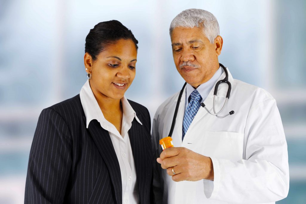 a pharmacist or medical staff person holding prescription medicine bottle while talking to patient