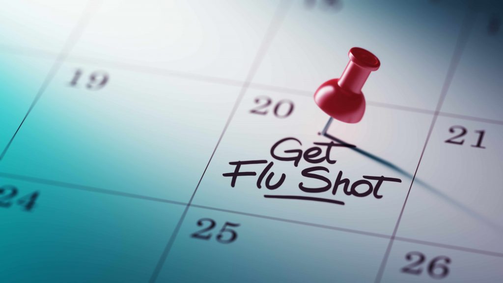 a close-up of a calendar, with a red push pin and the words GET FLU SHOT written on one date square