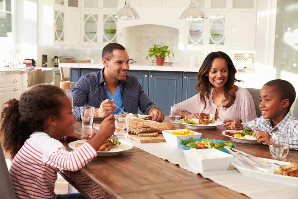 Young family of four eating breakfast together, adult male and female smiling at young boy, young boy smiling at girl