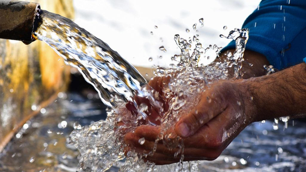 a man rinsing and washing his hands in water from a rusty pipe