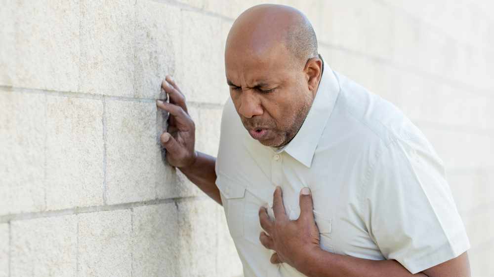 a middle-aged African American man holding his chest and leaning against a wall, maybe a heart attach or stroke