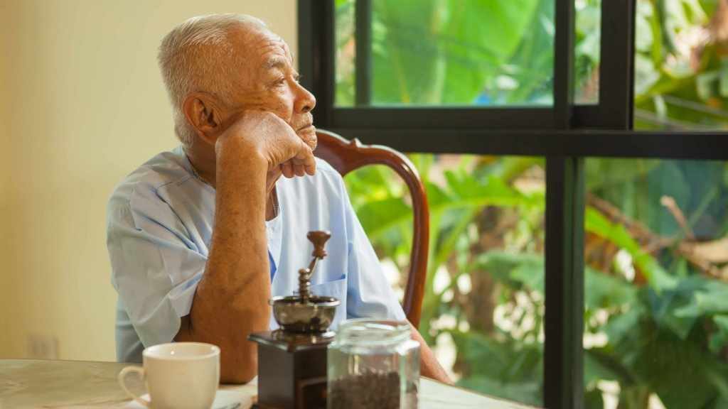 Un anciano está sentado a la mesa y mira por la ventana en silencio