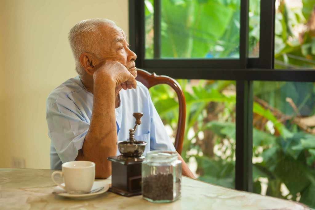 an older man sitting at a table, quietly staring out the window