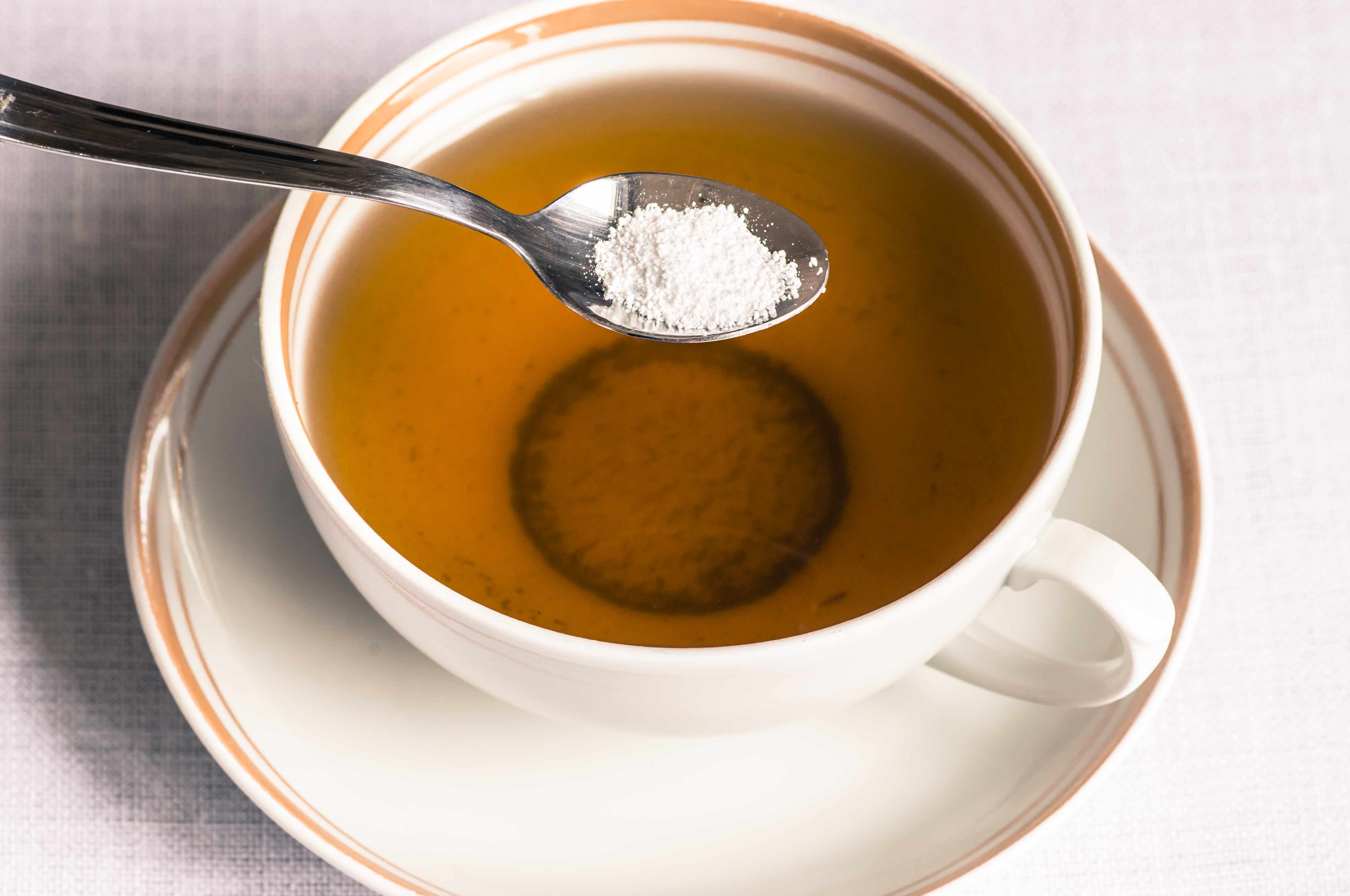 a spoonful of artificial sweetener being put in a cup of tea