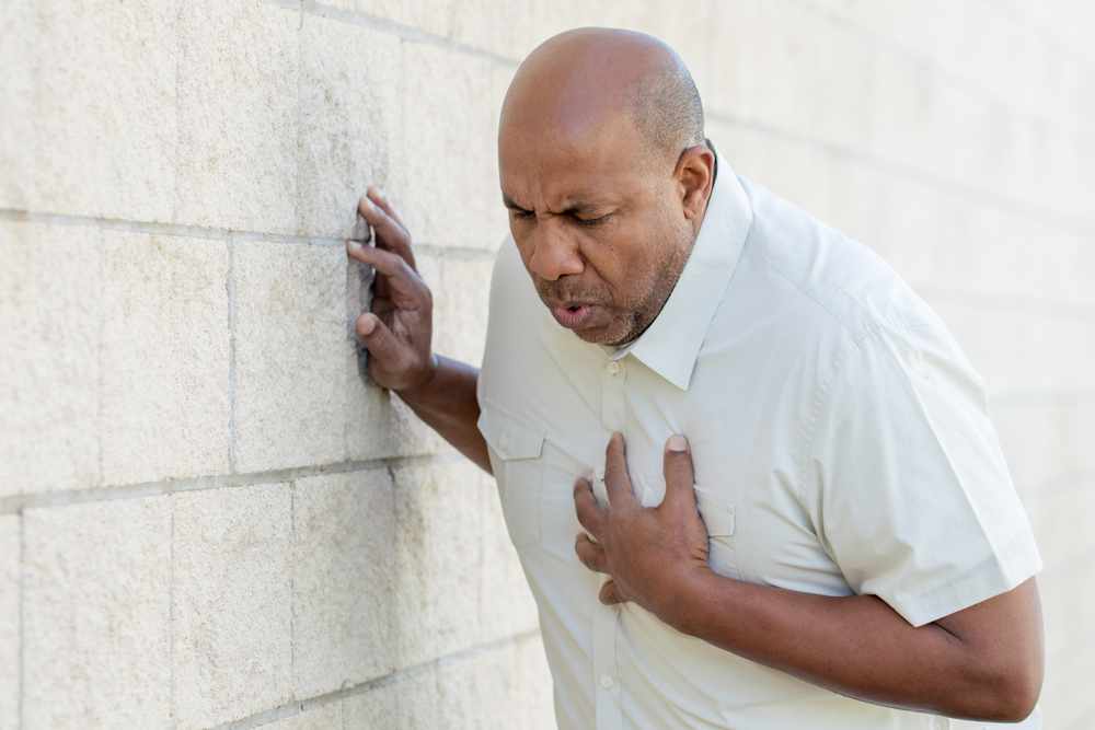 a middle-aged African American man holding his chest and leaning against a wall, maybe a heart attack or stroke