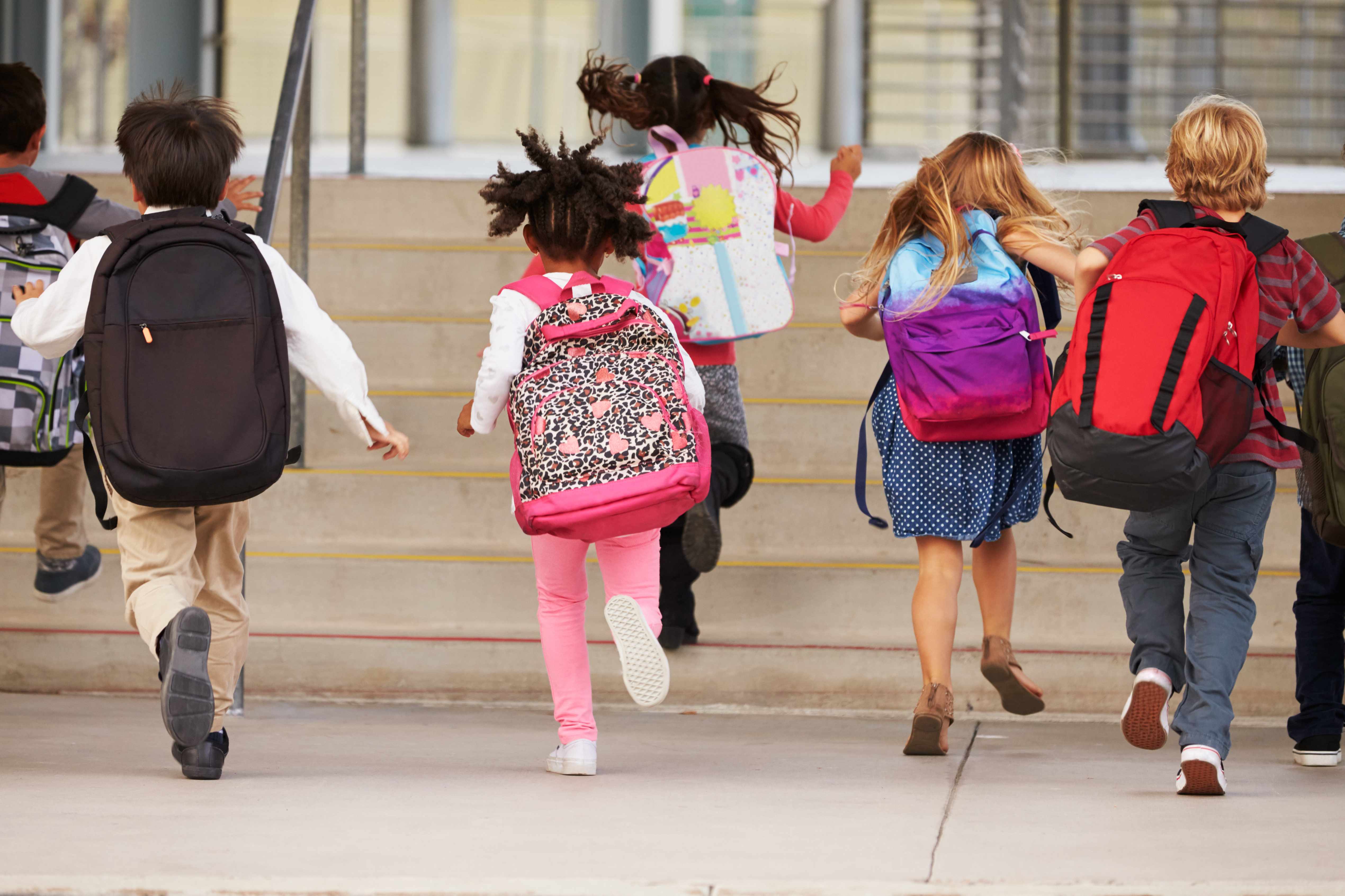 a group of elementary students running up the stairs wearing backpacks