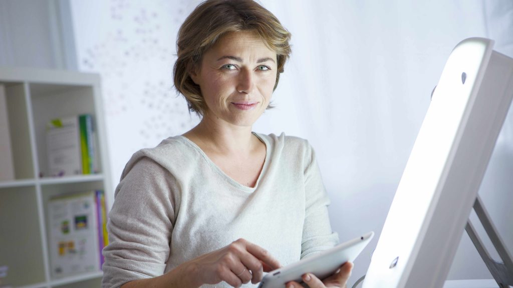 woman sitting with a light therapy lamp for SAD or depression