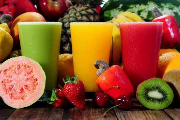 Various whole fruits and three glasses of juice smoothie