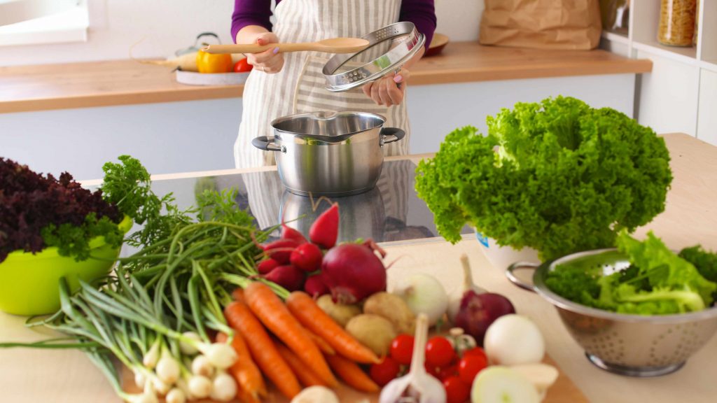 a woman cooking in a kitchen with a wide variety of healthy food choices on the counter, vegetables