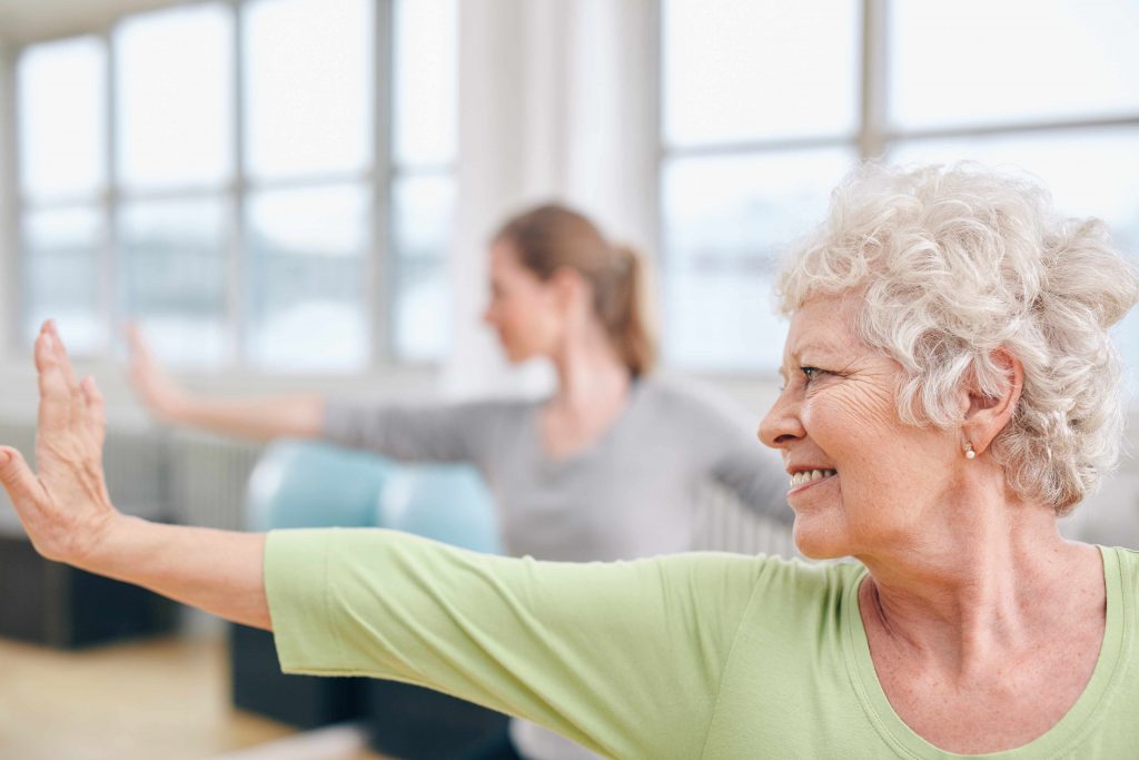 a close-up of a smiling older woman doing stretching exercises in a gym