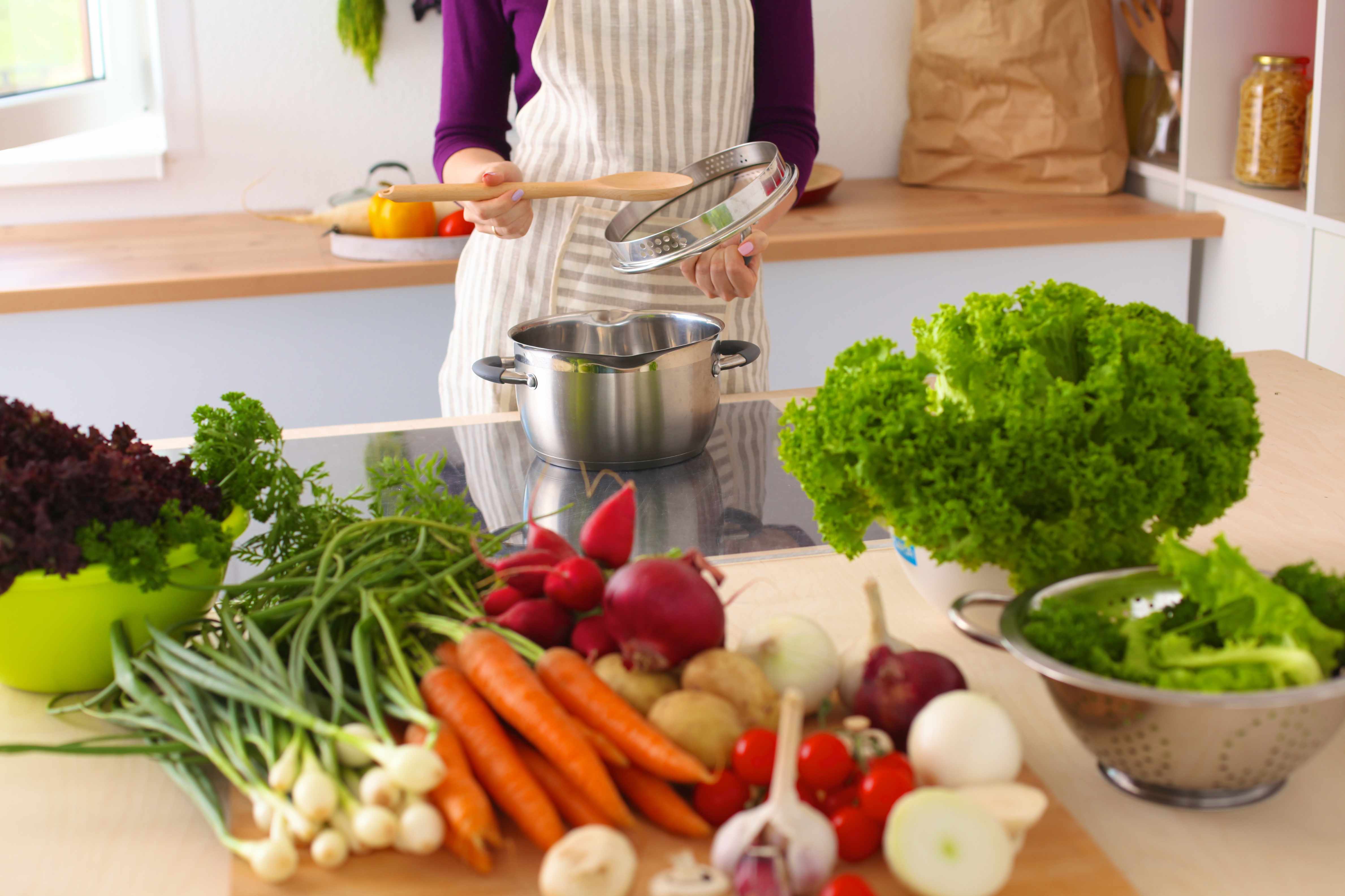 a woman cooking in a kitchen with a wide variety of healthy food choices on the counter, vegetables