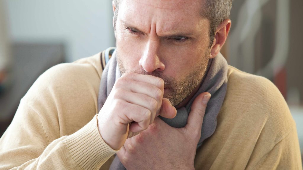 a Caucasian man with a scarf and coughing
