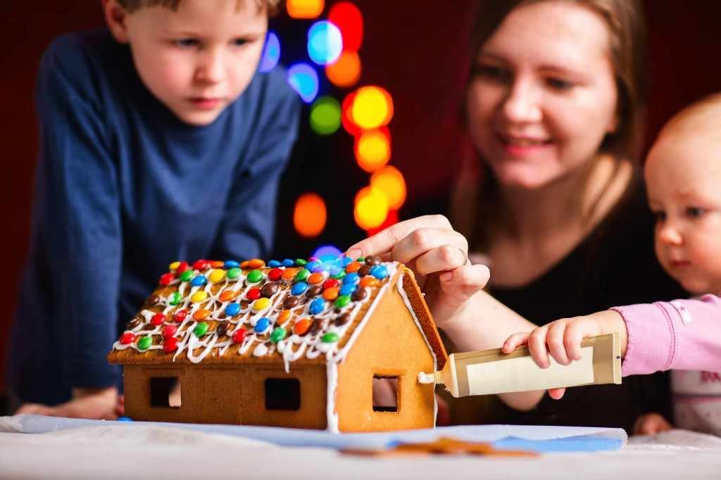 mother and children decorating holiday gingerbread house