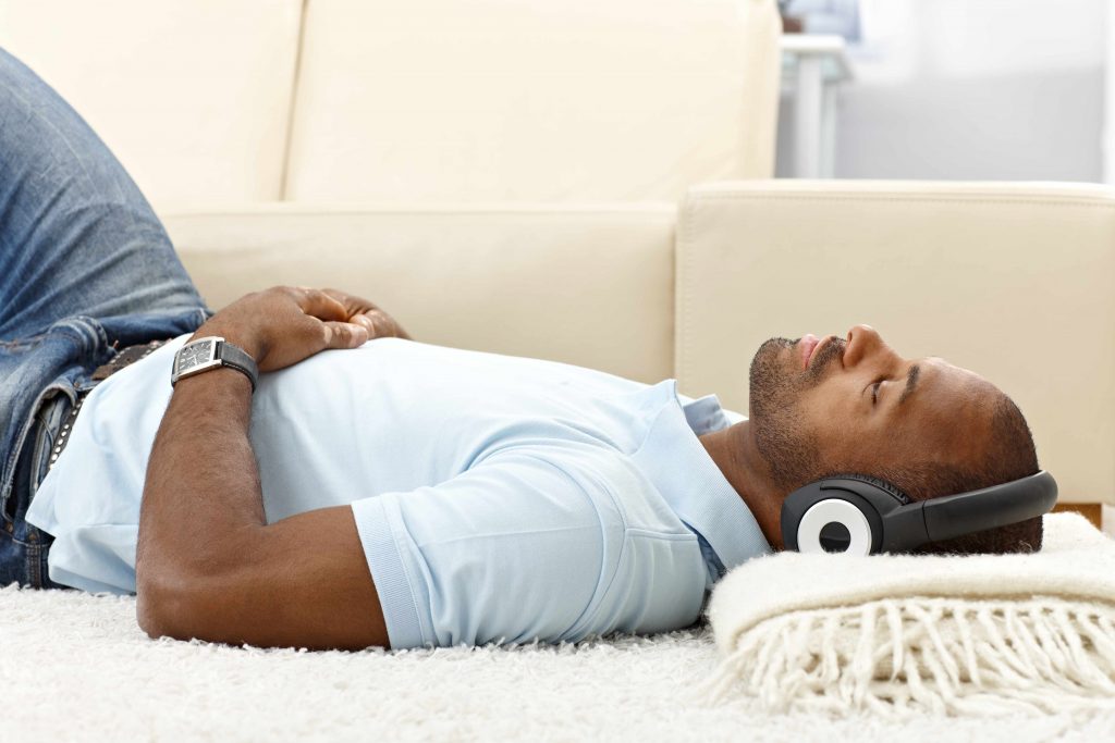 a young man lying on the floor, with his head resting on a folded blanket, peacefully listening to music with headphones