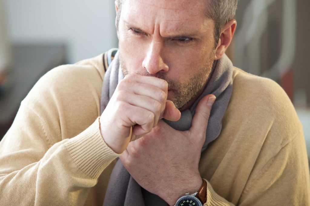 a Caucasian man with a scarf and coughing