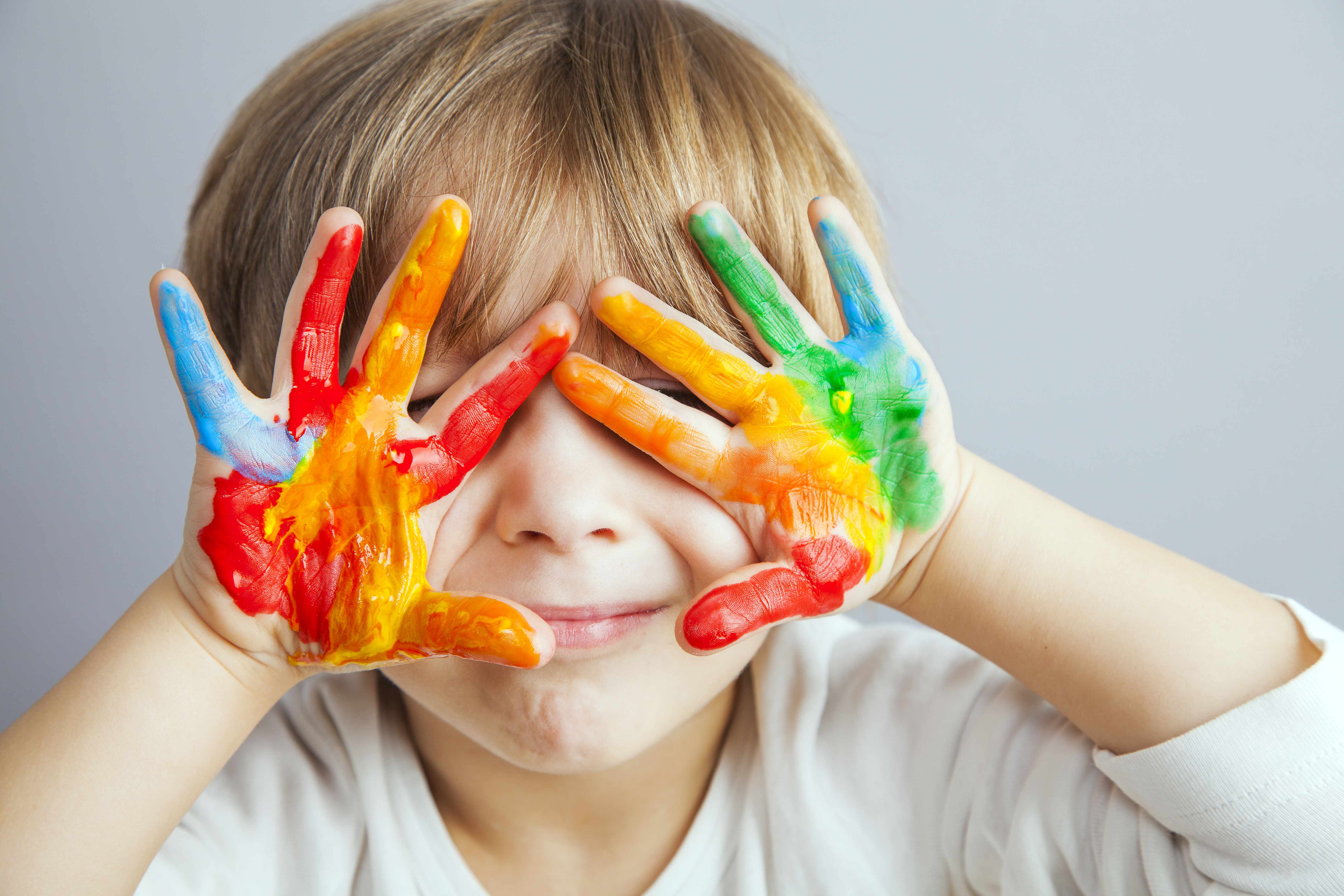 a little boy holding his messy paint covered hands over his face