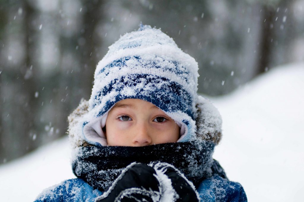 a cold little boy bundled up in winter clothes with snow falling