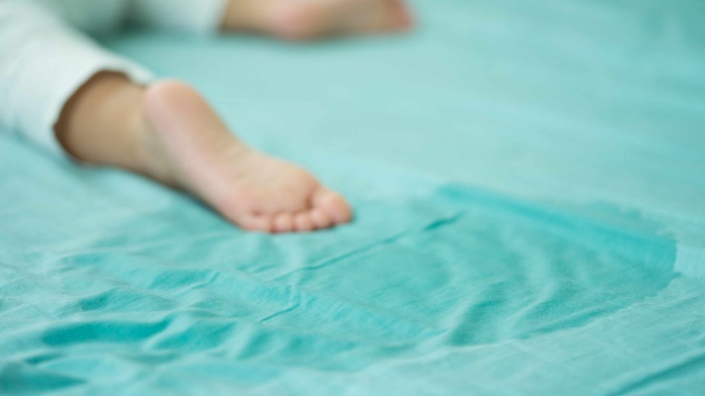 a child asleep on a light blue bed sheet with a wet spot