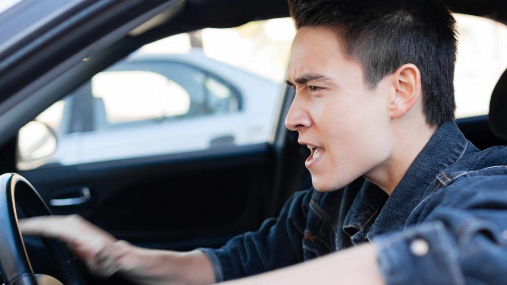 a young, angry man driving in a car demonstrating road rage behind the wheel. 