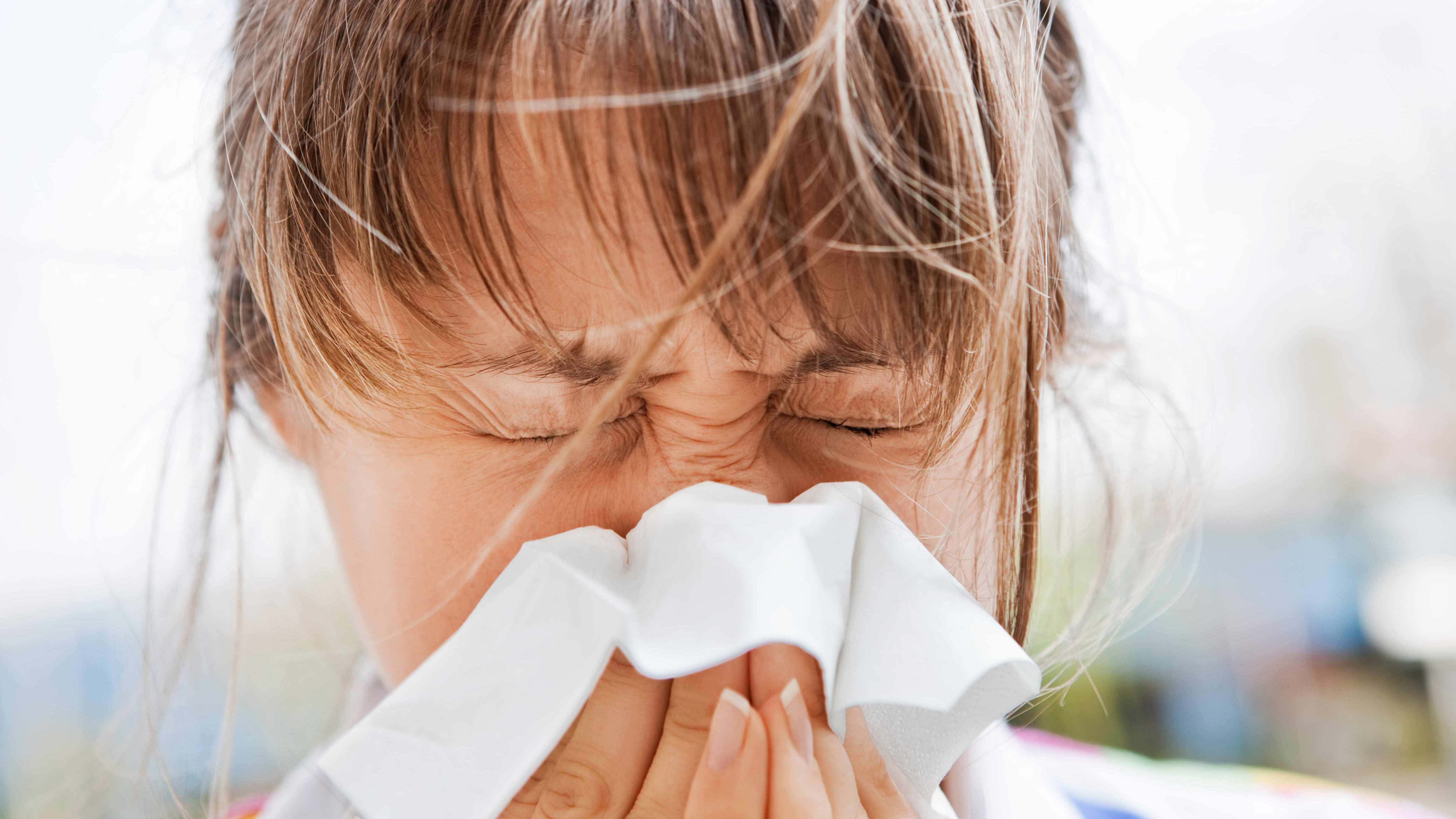 a young woman with a cold or allergies, sneezing into a tissue