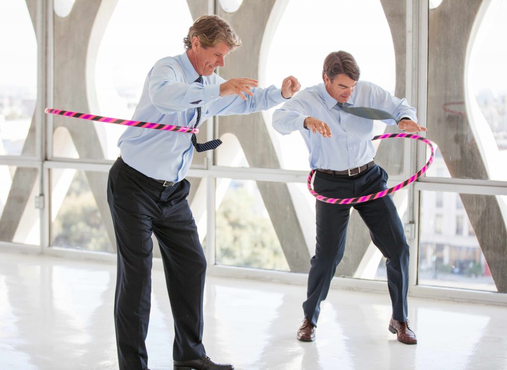 two men in suit pants, dress shirts and ties hula hooping