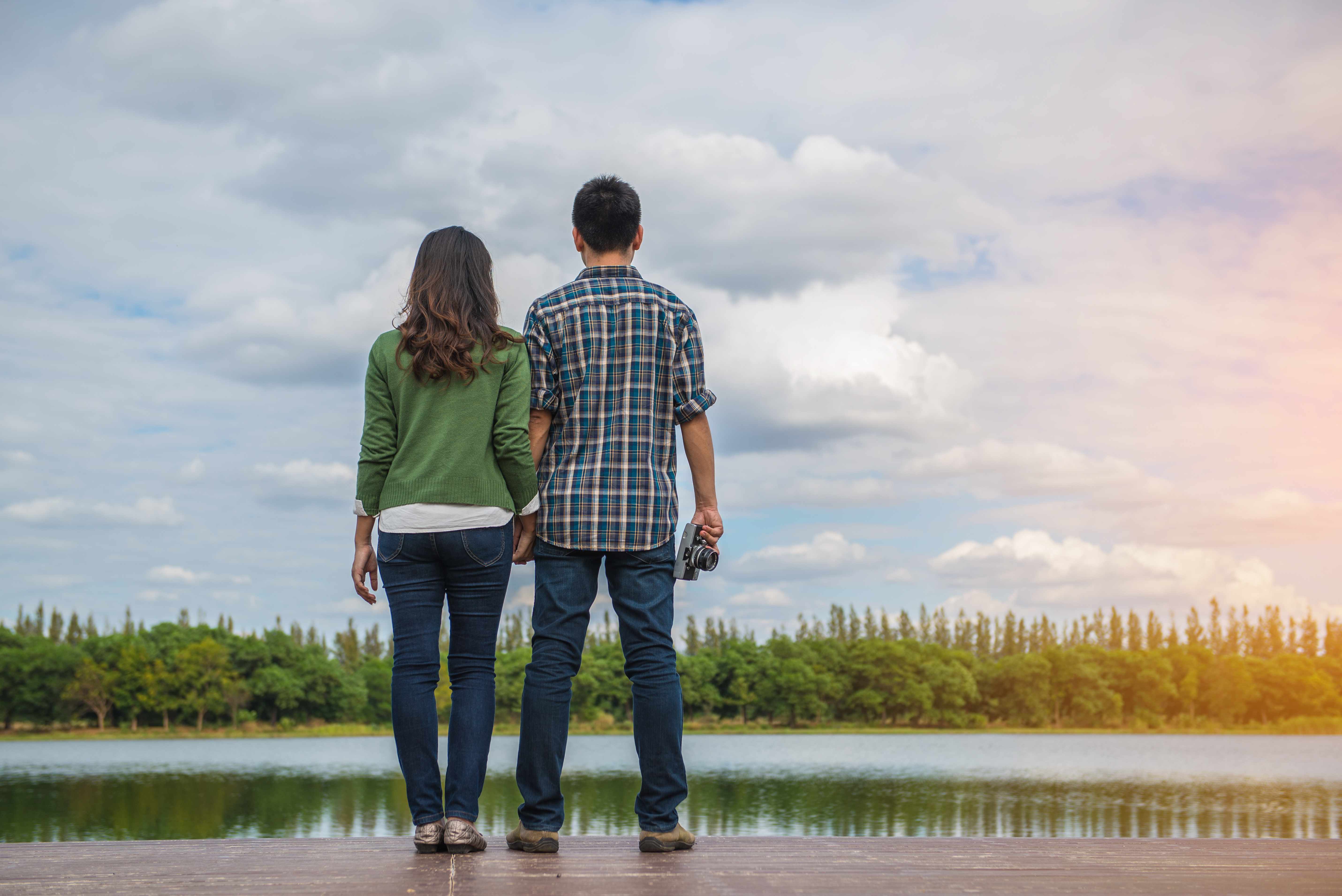 a couple standing on the edge of a lake looking at the landscape