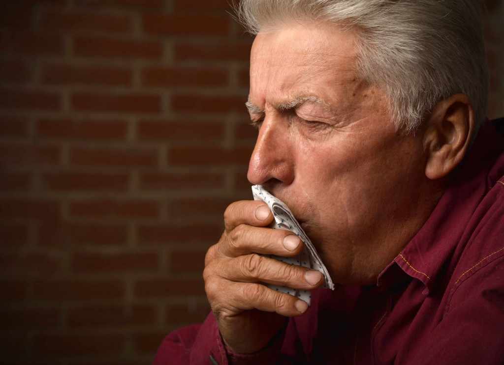 Elderly man coughing into a napkin