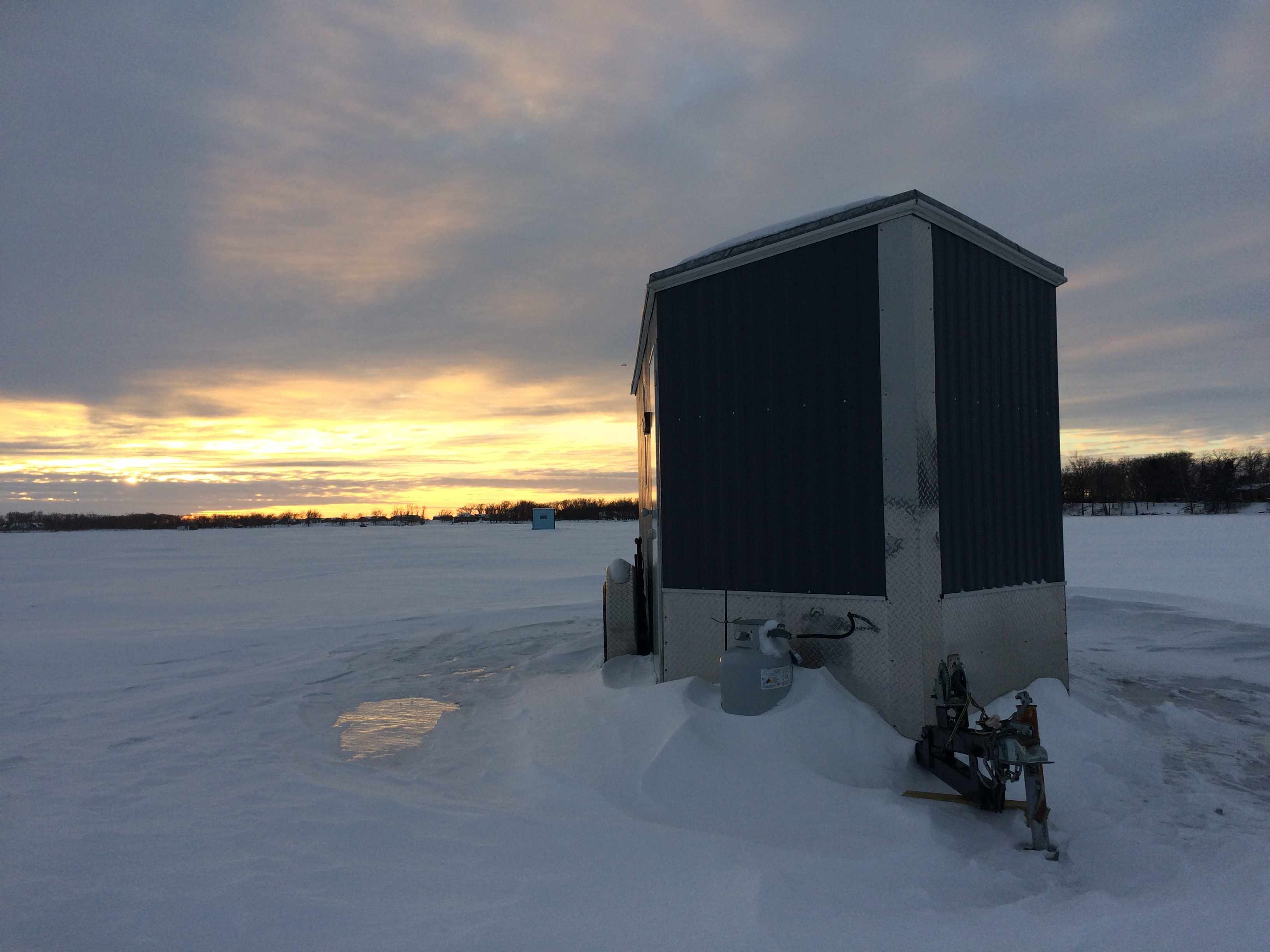 sunset on a frozen lake with ice fishing house in foreground