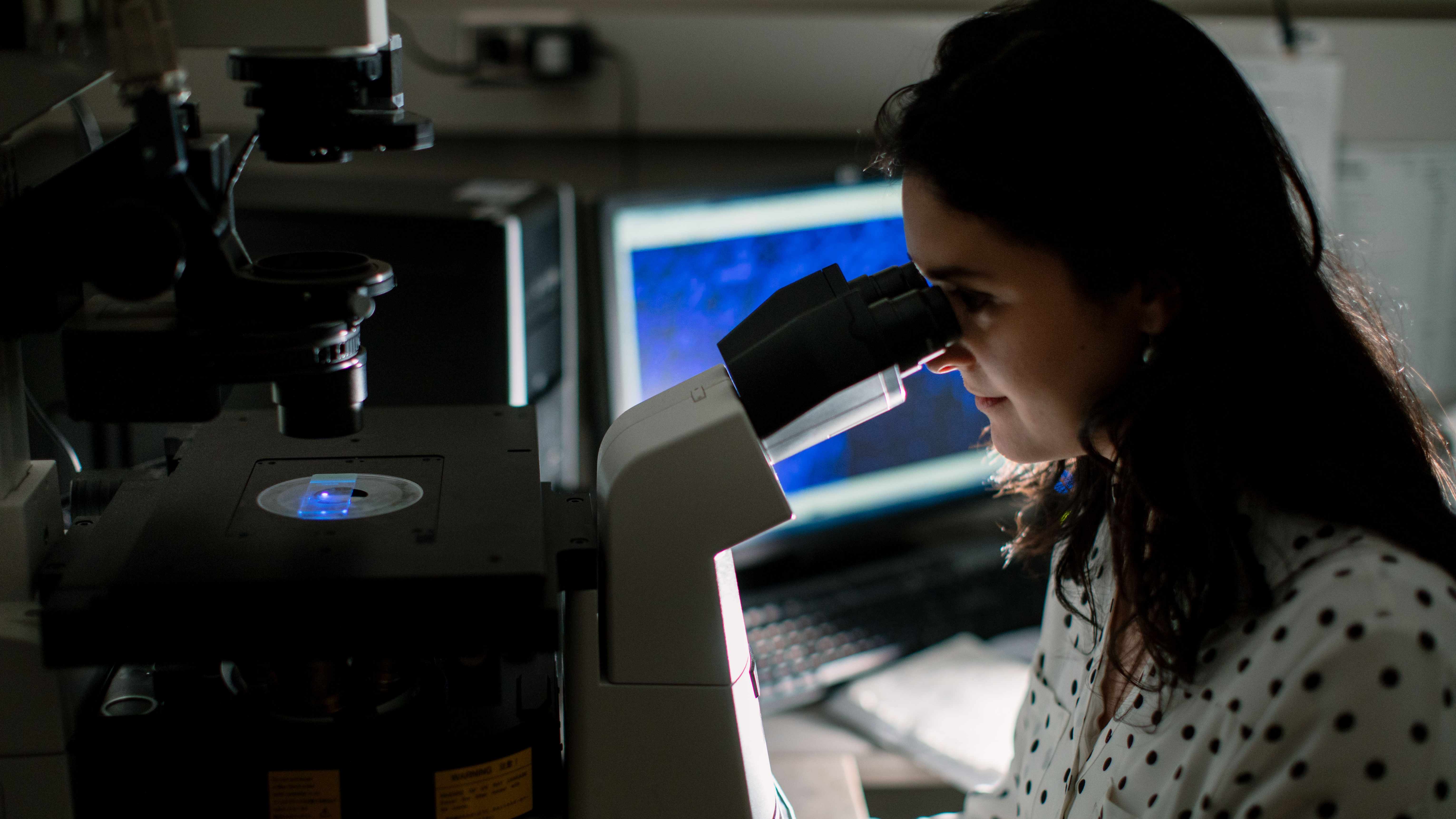 Una investigadora observa una lámina bajo el microscopio.