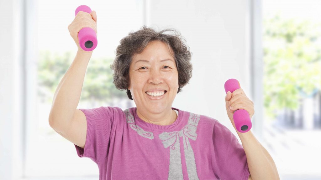 Una mujer mayor sonríe mientras hace ejercicios con pesas de mano