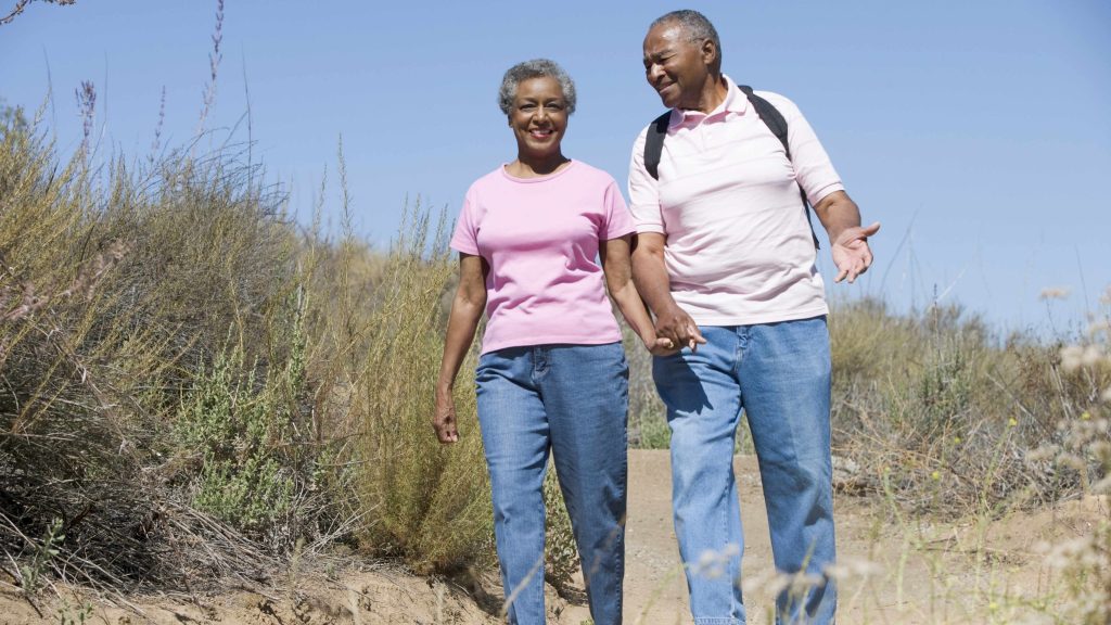 an African-American middle-aged couple holding hands and walking, exercising on the beach