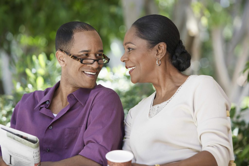 a middle-aged couple sitting outside, looking at one another and smiling