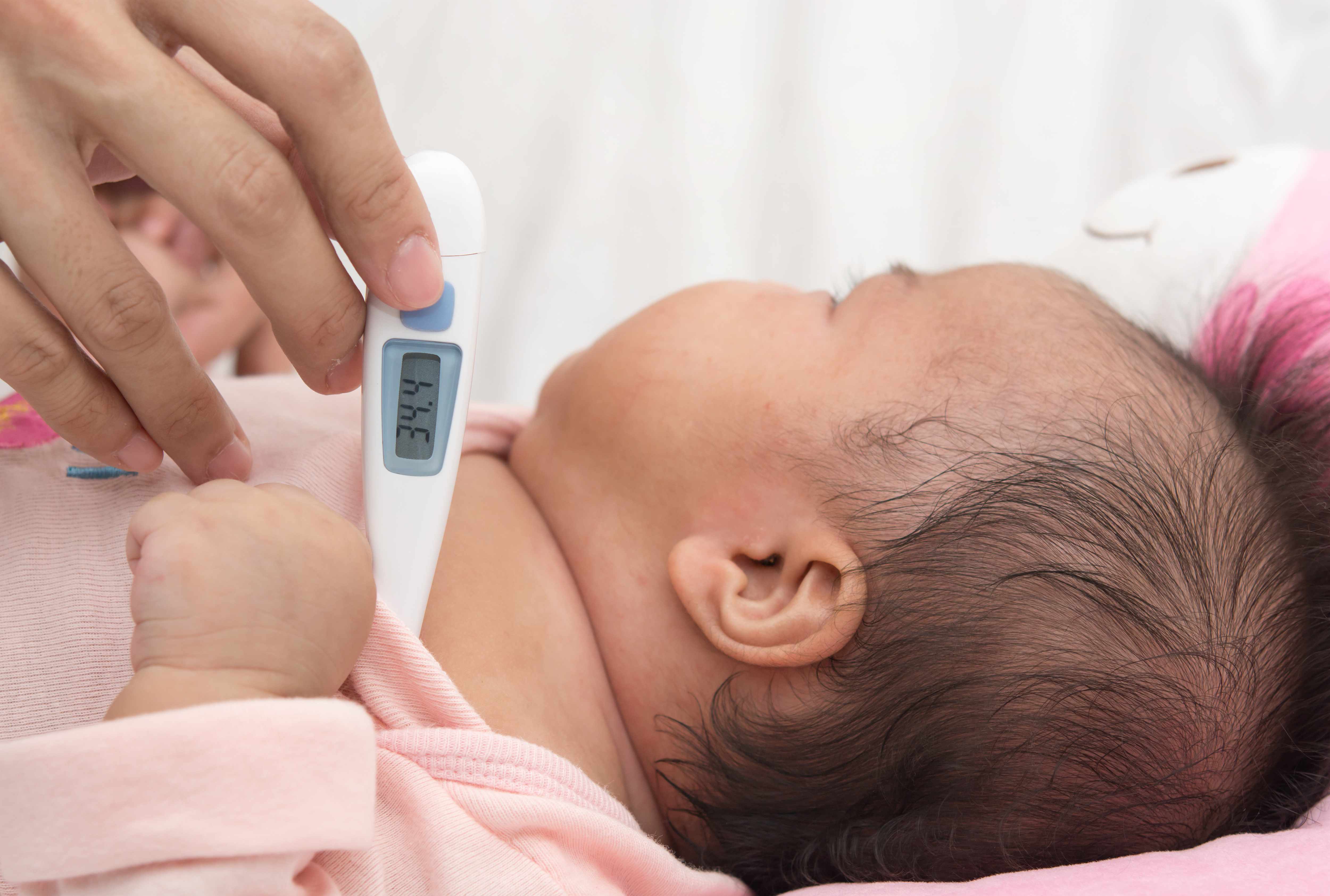 an infant having his or her temperature taken with a digital thermometer under the arm
